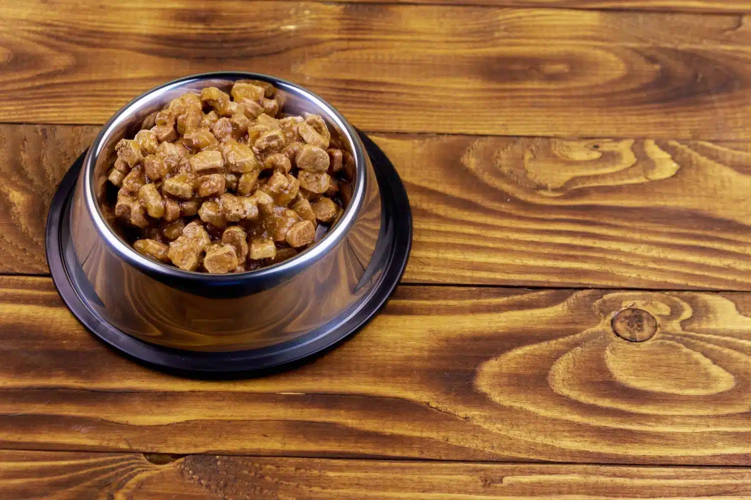 A bowl of wet dog food on a wooden table.